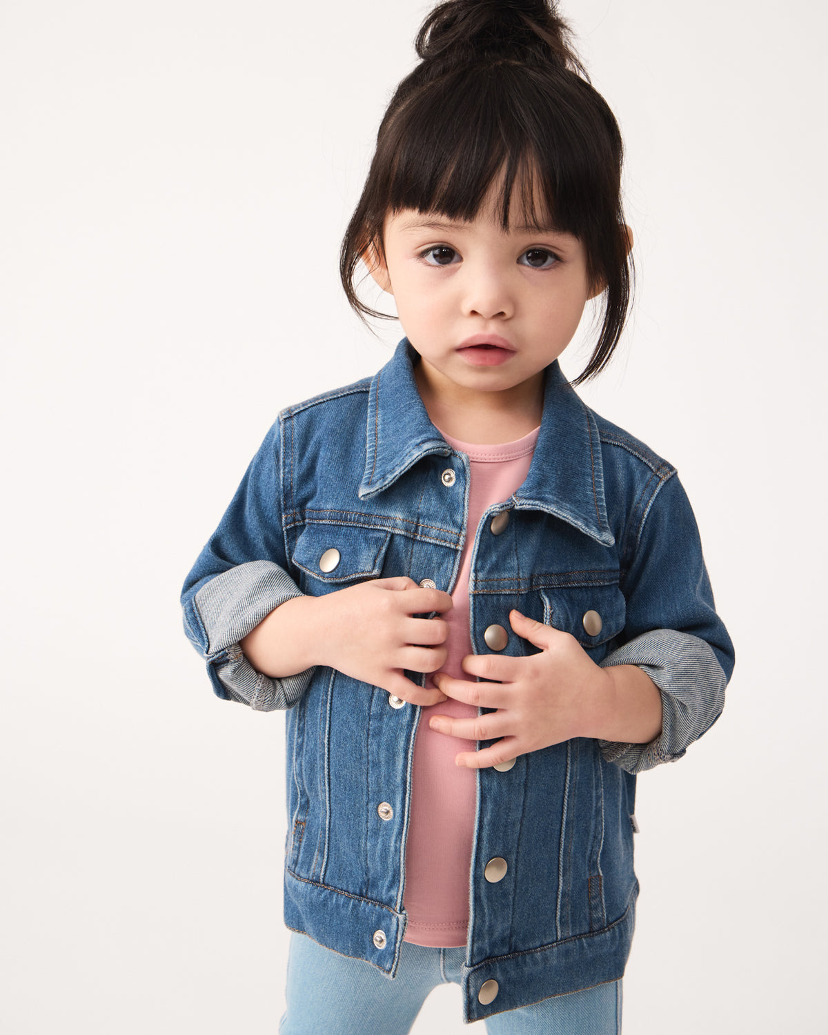 Girl wearing the Midwash Blue Denim Trucker Jacket layered over a mauve blush tee