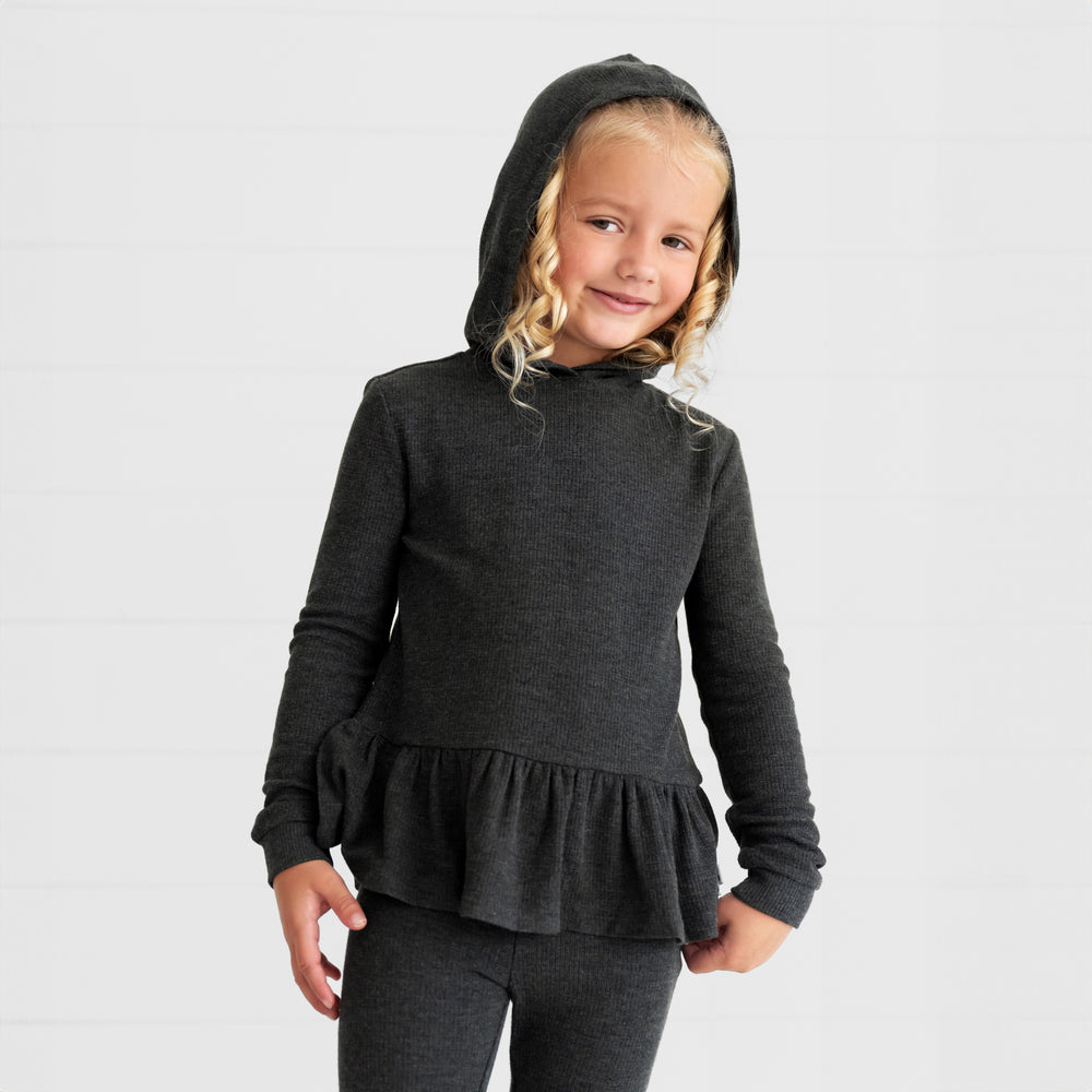 Close up image of a child wearing a Heather Black Waffle Peplum Hooded Tee with the hood up and matching Waffle Flare Pants