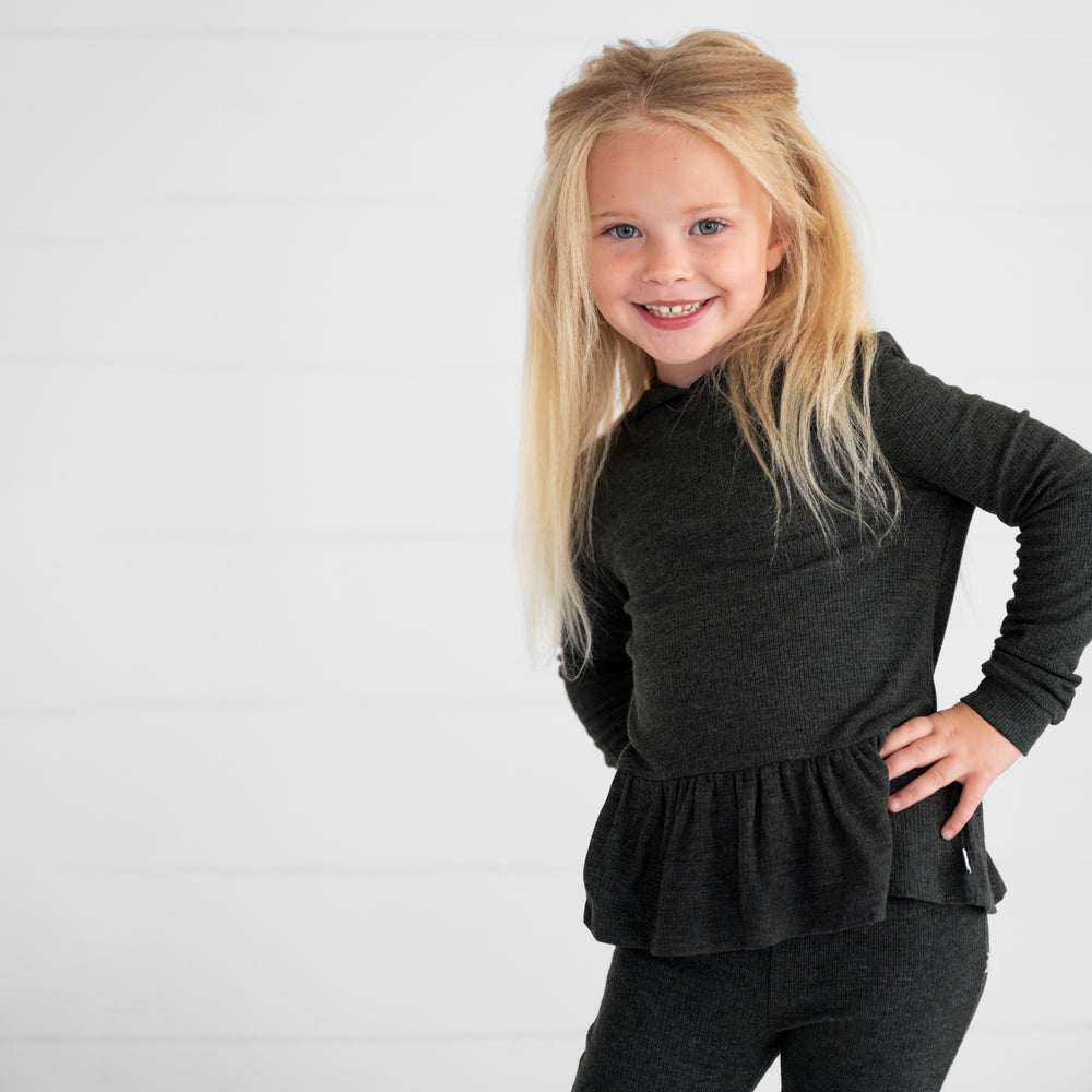 Close up image of a child wearing a Heather Black Waffle Peplum Hooded Tee and Waffle Flare Pant