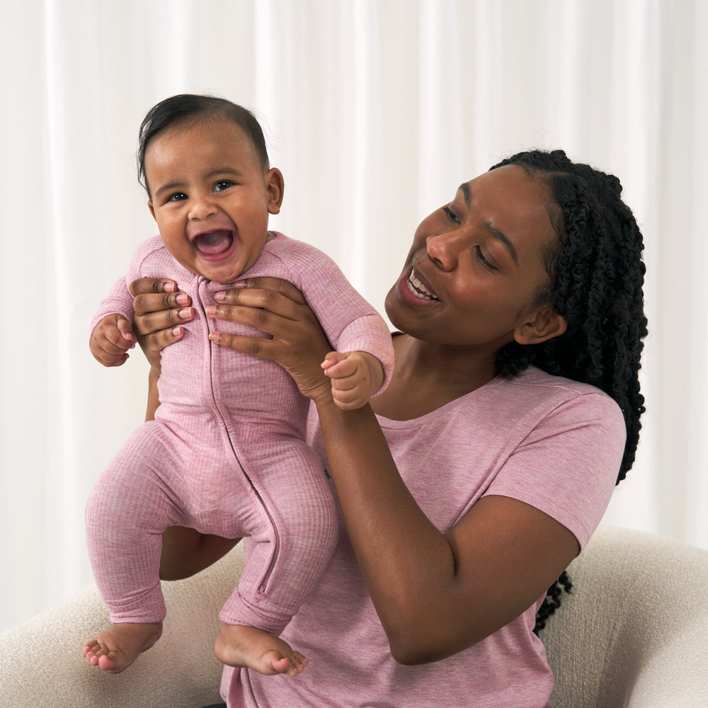 Image of a woman wearing a Heather Mauve women's nursing top holding up her child wearing a matching Heather Mauve zippy