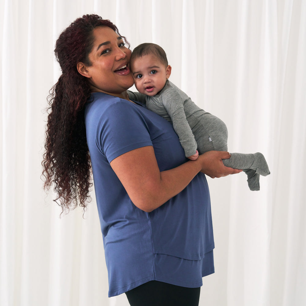 profile view of a woman wearing an Indigo women's nursing top holding up her child wearing a Heather Gray zippy