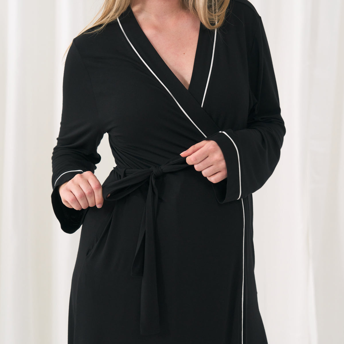 Close up image of a woman wearing a solid black women's robe showing off the tie closure