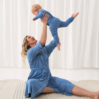 Woman wearing a heather Blue women's robe holding up her child wearing a matching Heather Blue two piece pajama set