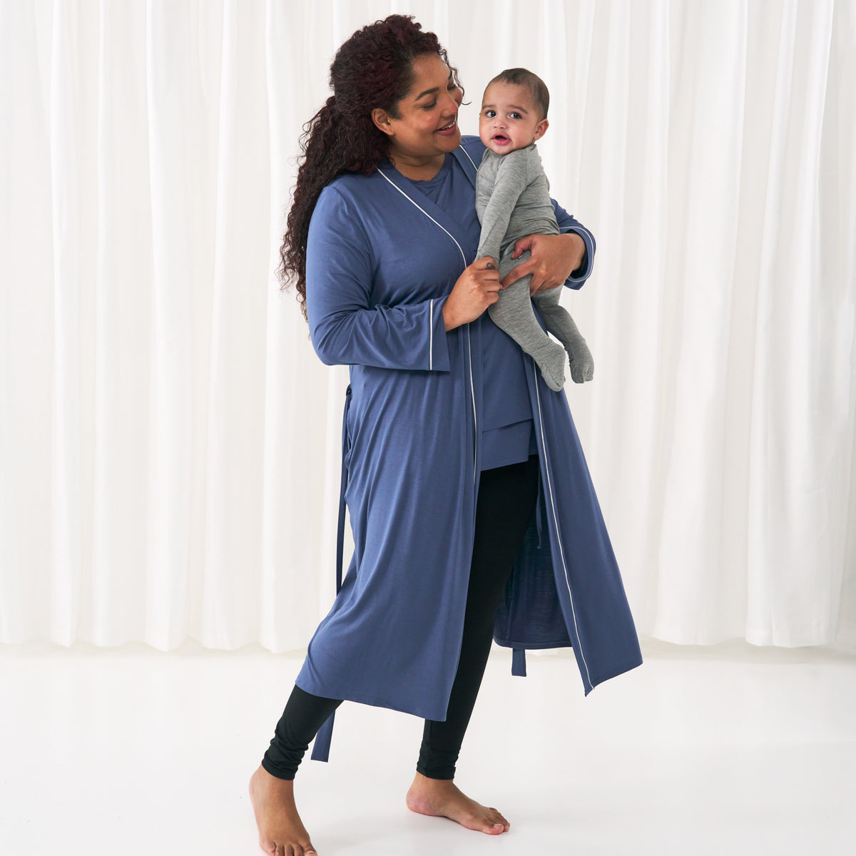 Woman holding her child. She is wearing an Indigo nursing top under a matching Indigo women's robe. Her child is wearing a Heather Gray zippy