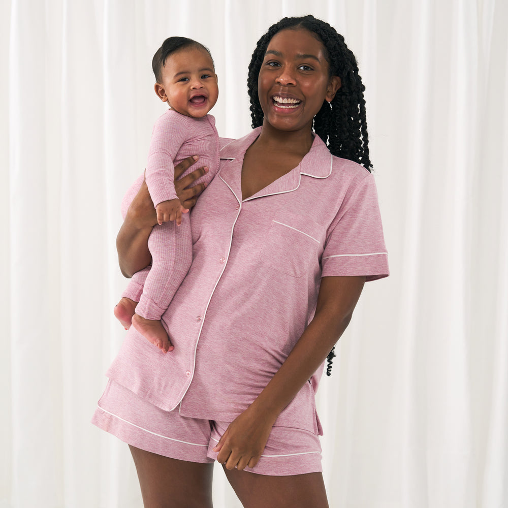 Image of a mom holding her child. Mom is wearing a Heather Mauve women's short sleeve and shorts pajama set. Her child is matching wearing a Heather Mauve short sleeve & shorts pajama set