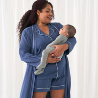 woman wearing an Indigo women's short sleeve and shorts pajama set an matching Indigo women's robe. She is holding her child wearing a Heather Grady zippy