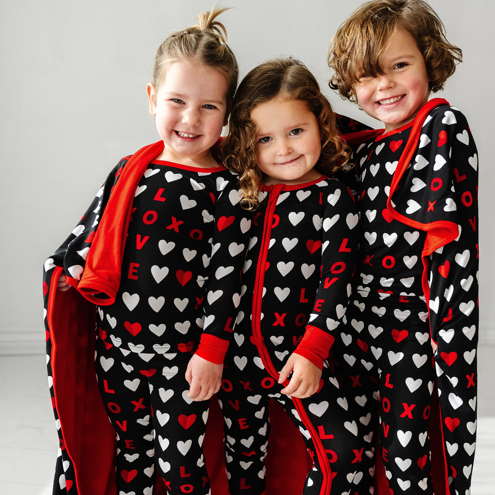Click to see full screen - Three children wearing Black XOXO printed pajamas cuddled under a Black XOXO large cloud blanket