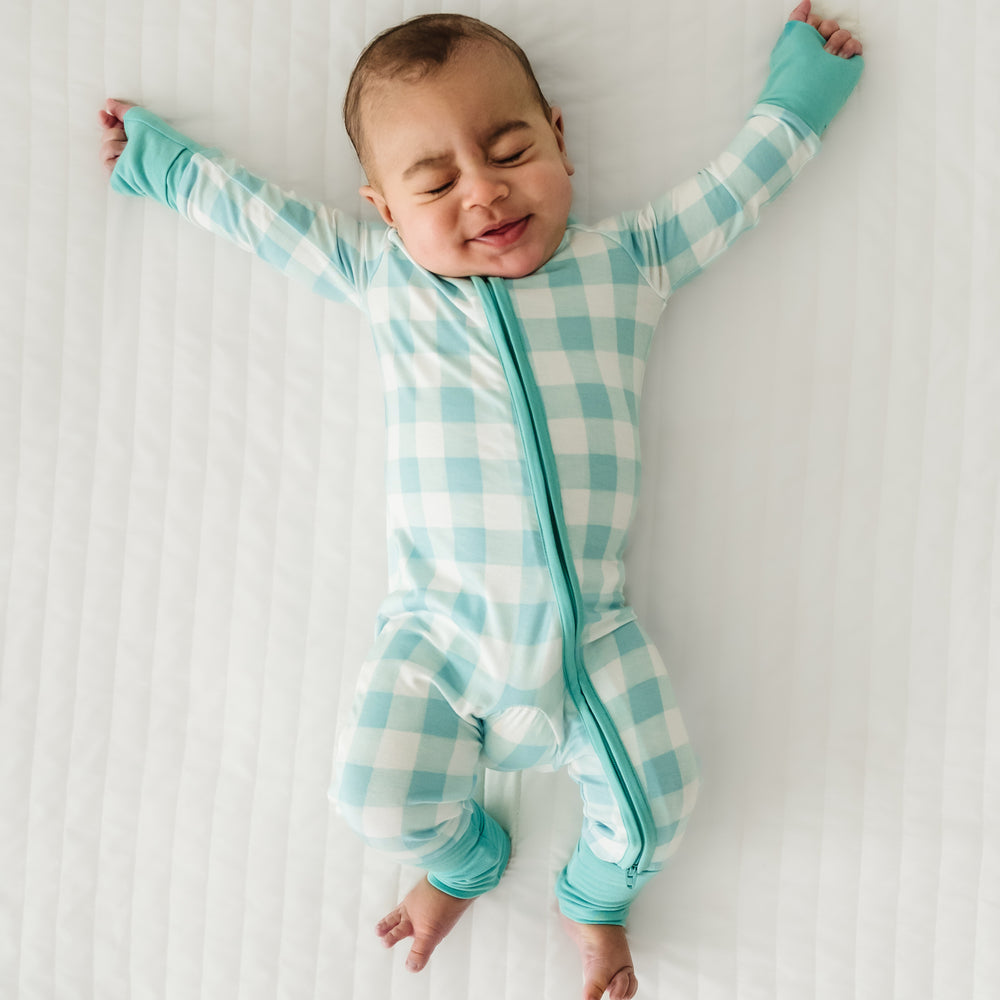 Click to see full screen - Child laying on a bed wearing a Aqua Gingham zippy