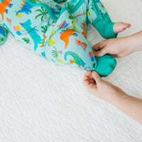 Child laying on a bed wearing a Prehistoric Party zippy. her mother is folding over a foot cuff
