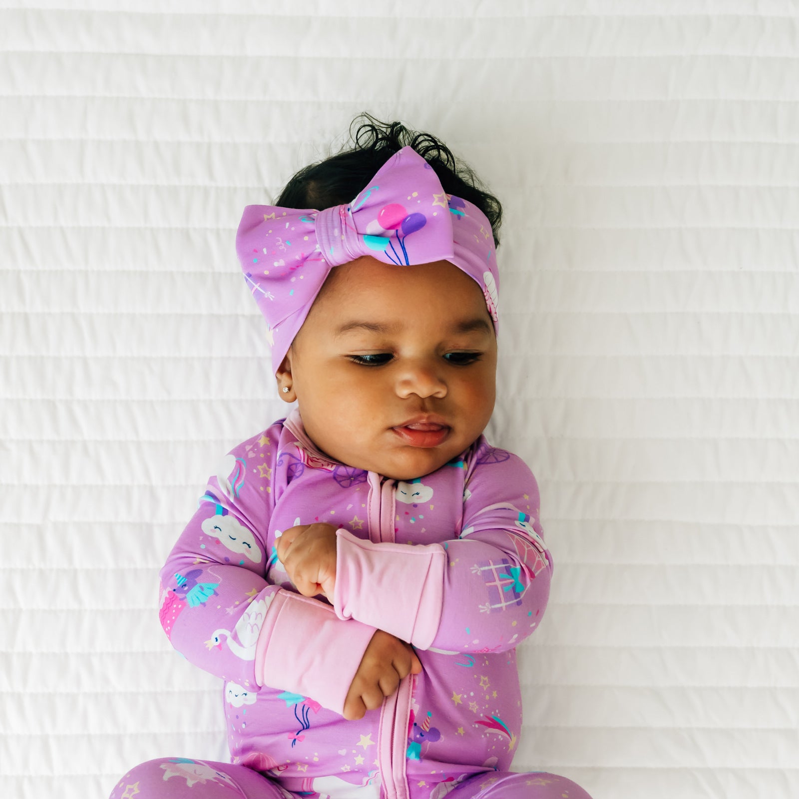 Child laying on a bed wearing a Magical Birthday zippy and matching luxe bow headband