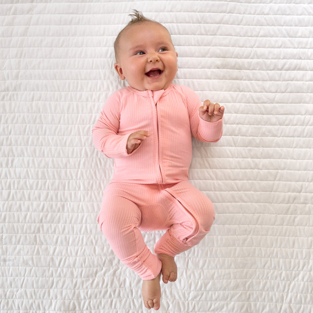 Top view image of baby laying down and smiling while in a Bubblegum Ribbed Zippy