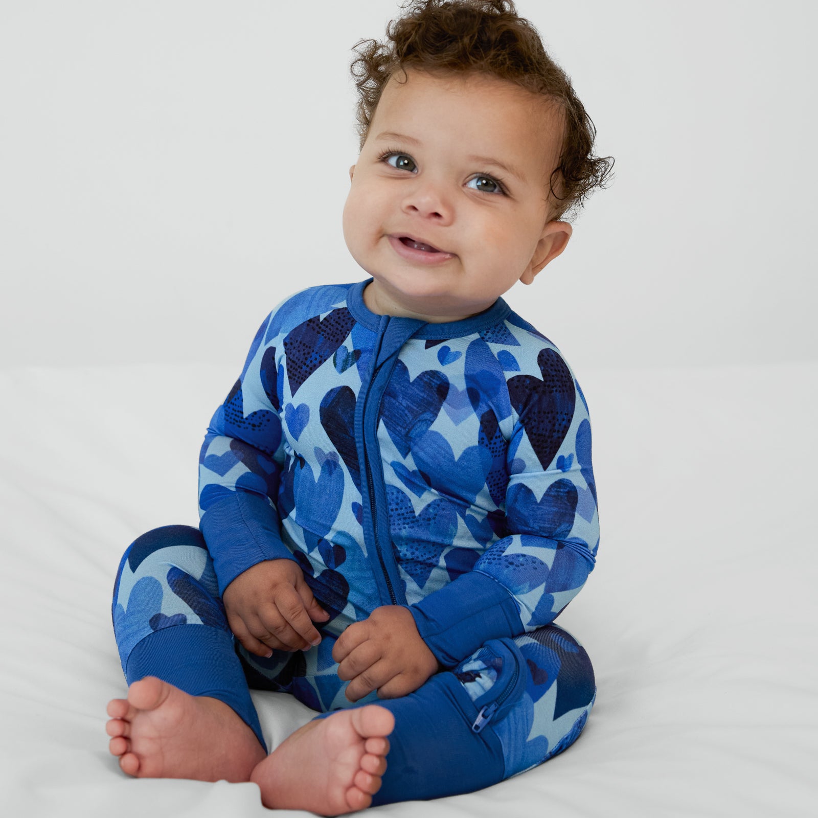 Baby boy sitting in Blue Hearts & Crafts zippy pajamas.