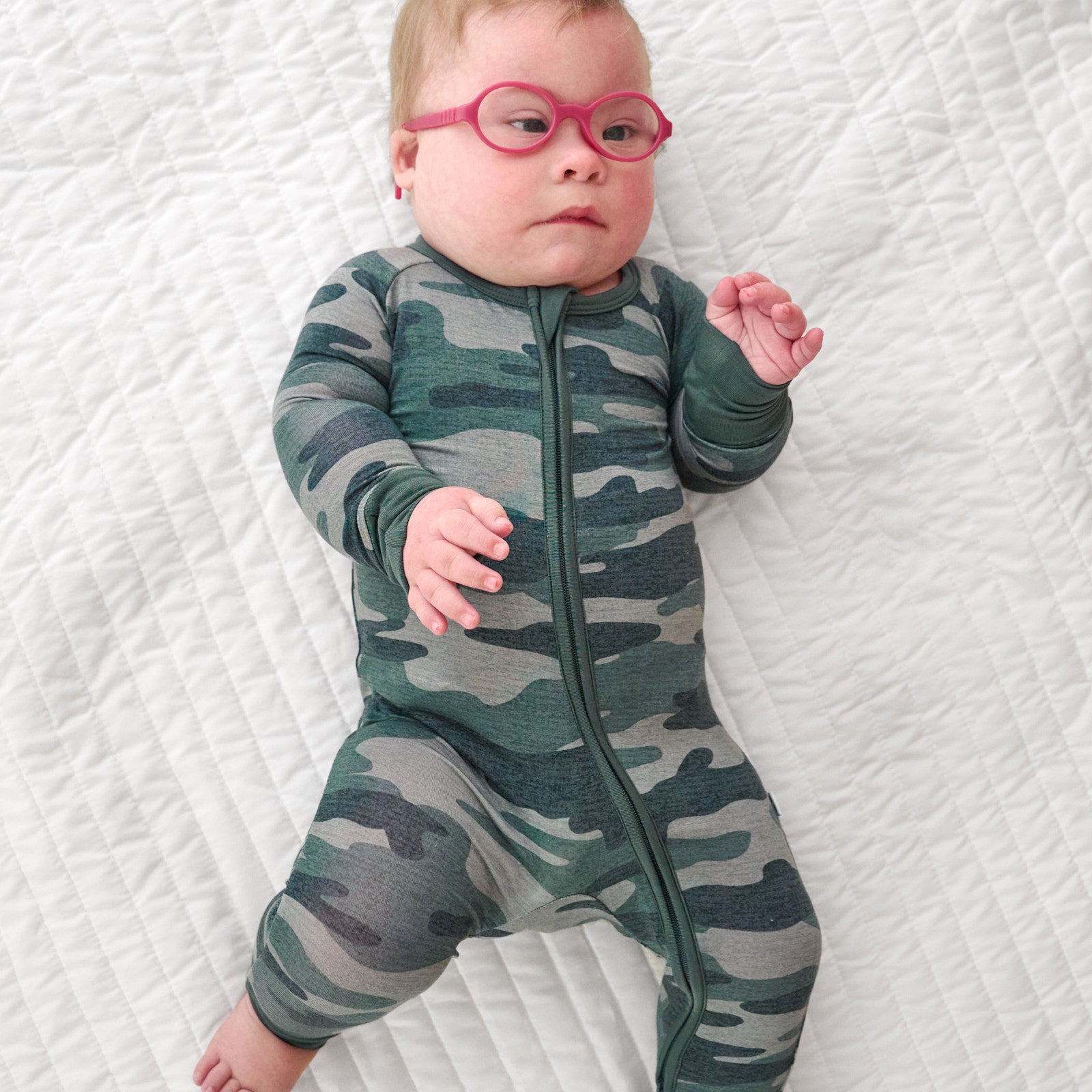 Top view image of baby laying down in glasses while wearing the Vintage Camo Zippy