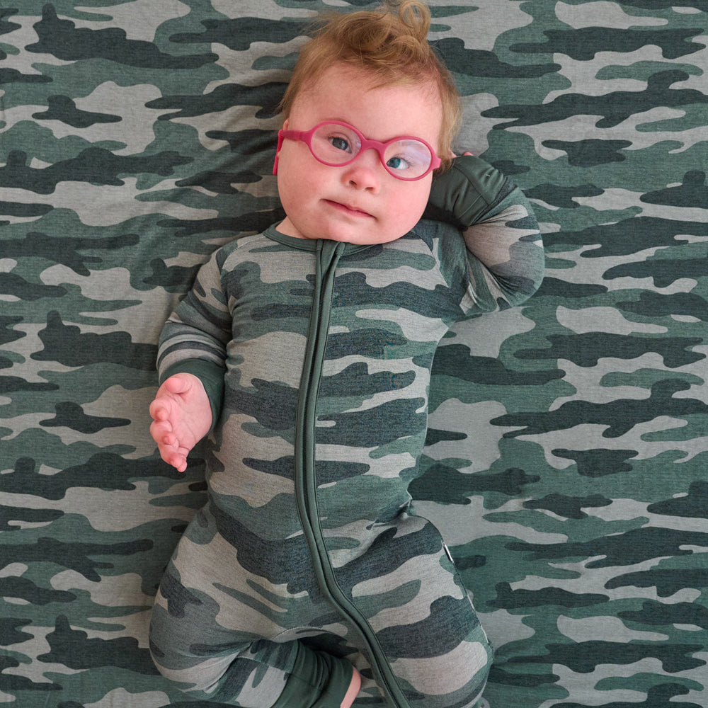 Top view image of baby in glasses laying down on the Vintage Camo Twin Sheet Set, while wearing the Vintage Camo Zippy