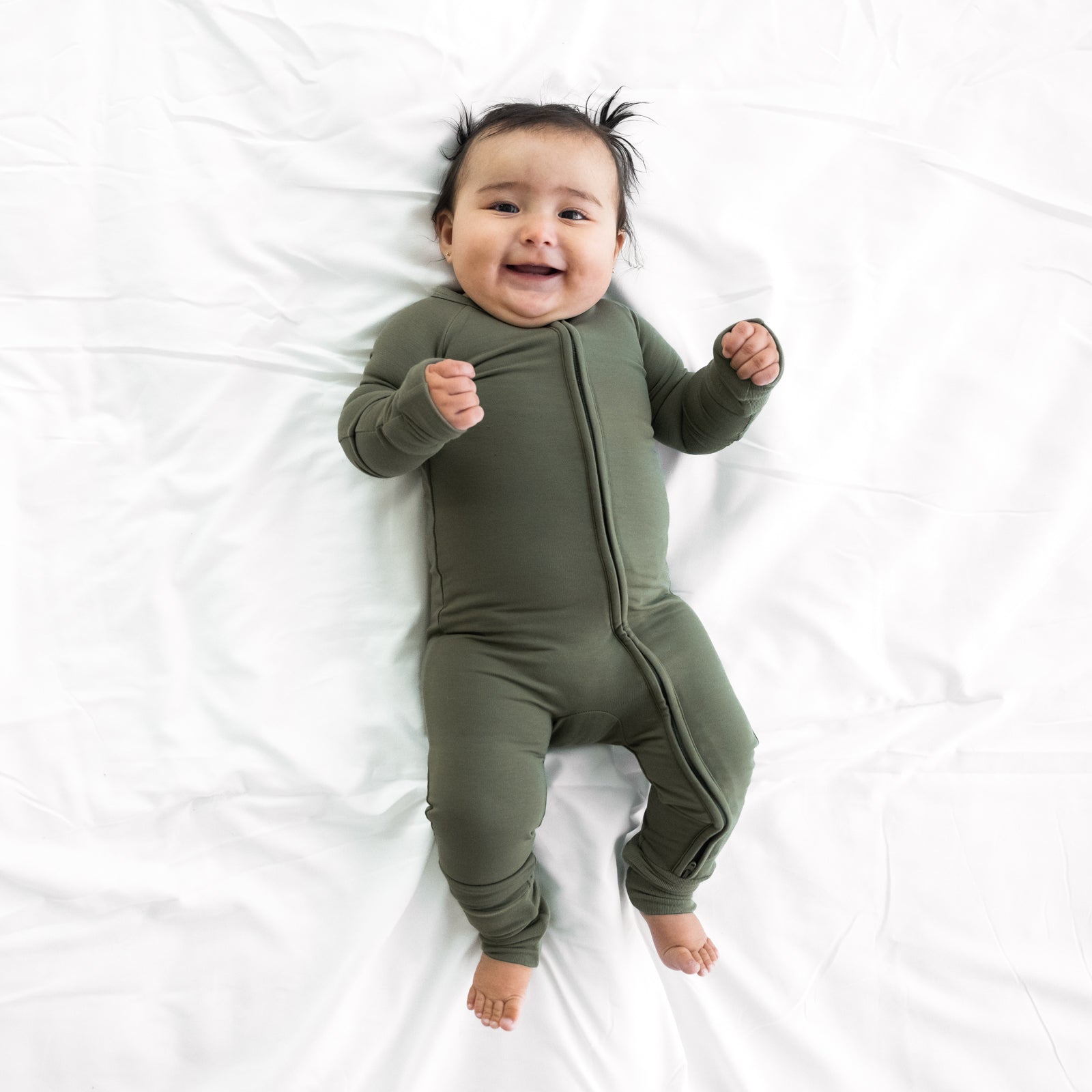 Child laying on a bed wearing a Cozy Olive zippy