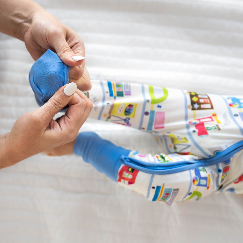 Alternate image of a child laying on a bed wearing an Education Express zippy. Mom is demonstrating the folded over foot cuff