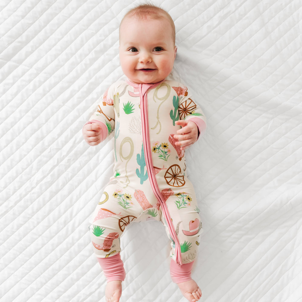 Child laying on a bed wearing a pink Ready to Rodeo zippy