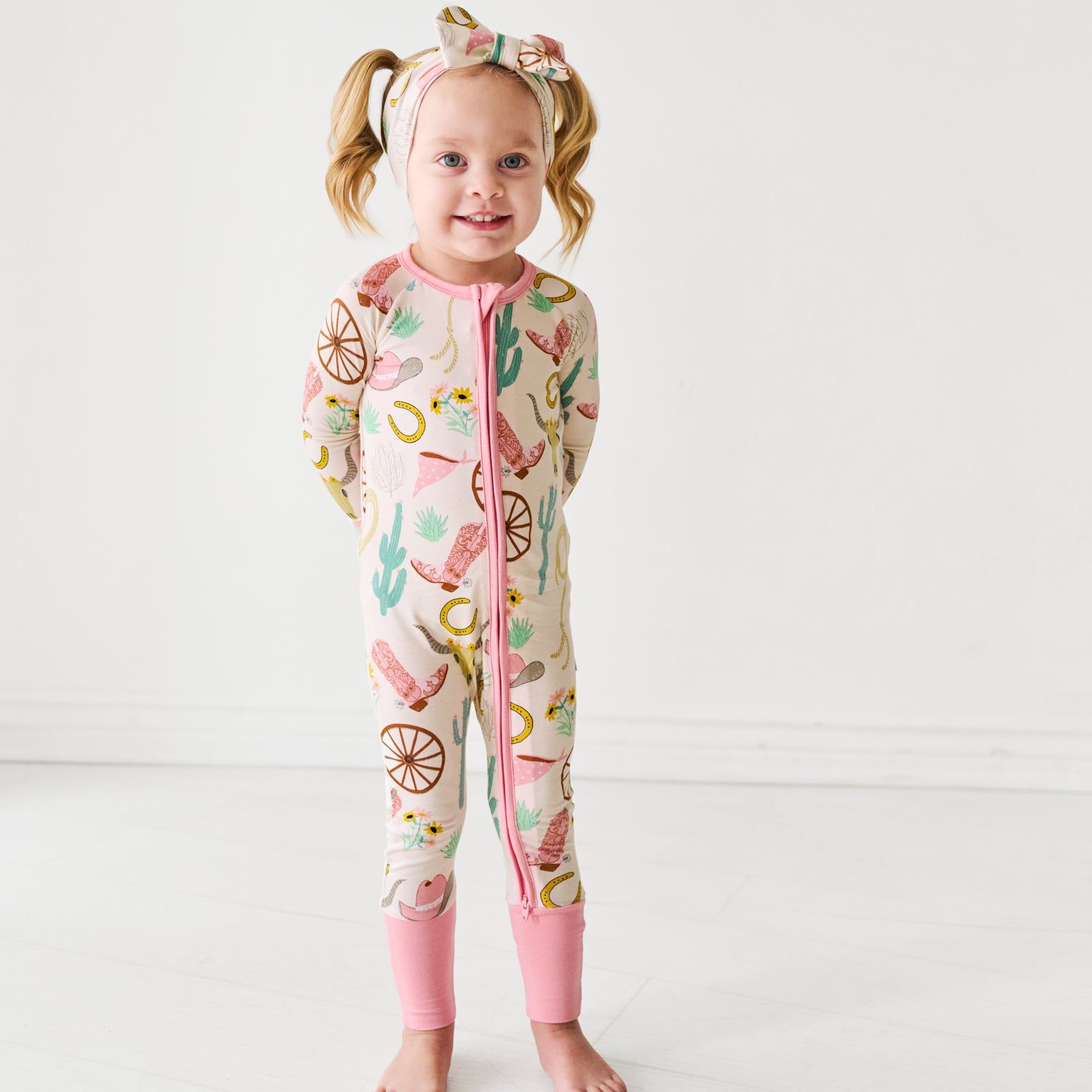 Child posing wearing a pink Ready to Rodeo zippy paired with a matching luxe bow headband