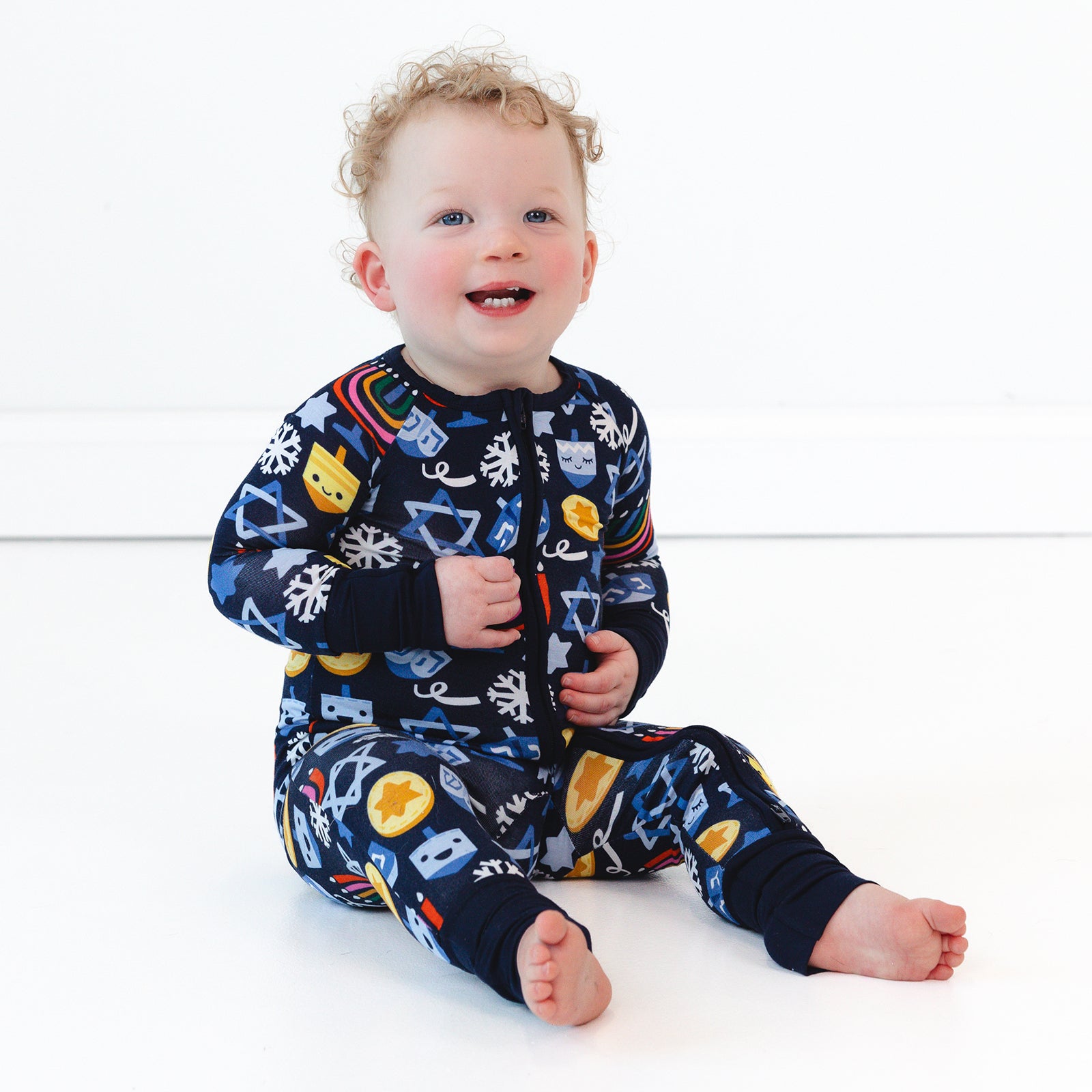 Child sitting on the ground wearing a Playful Dreidels Zippy