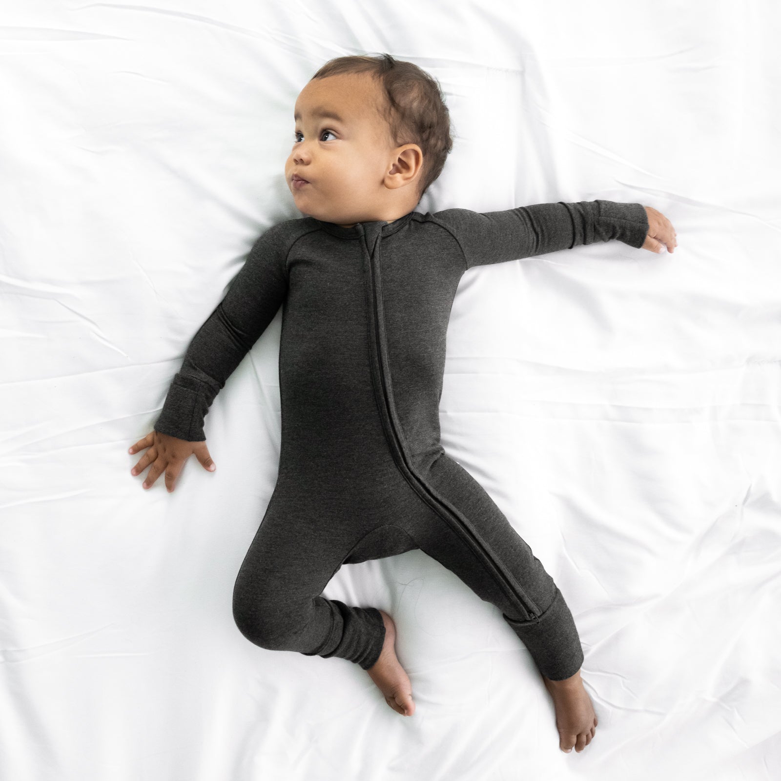 Child laying on a bed wearing a Cozy Heather Black zippy