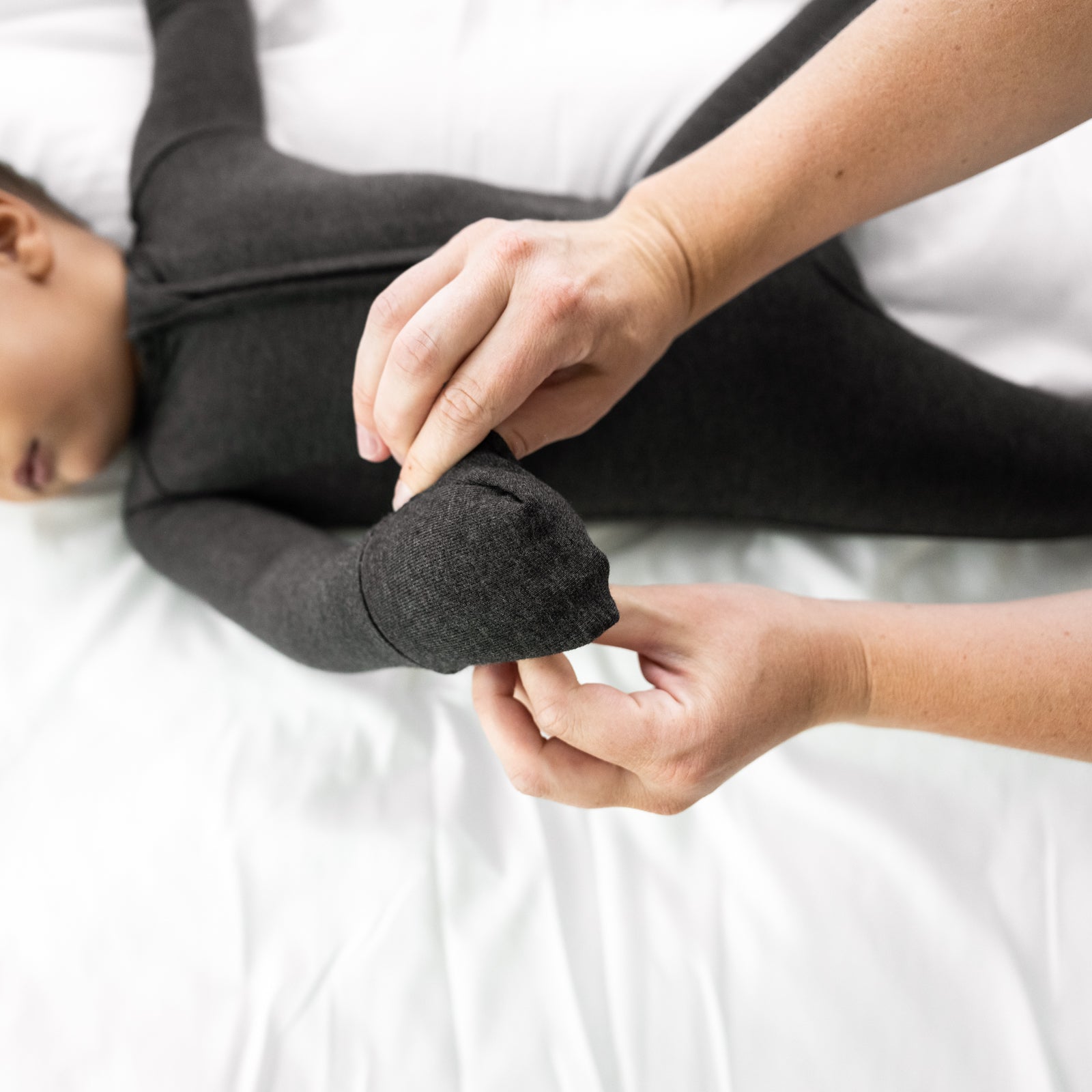 Child laying on a bed wearing a Cozy Heather Black zippy. Mother is detailing the folded over mitten cuff