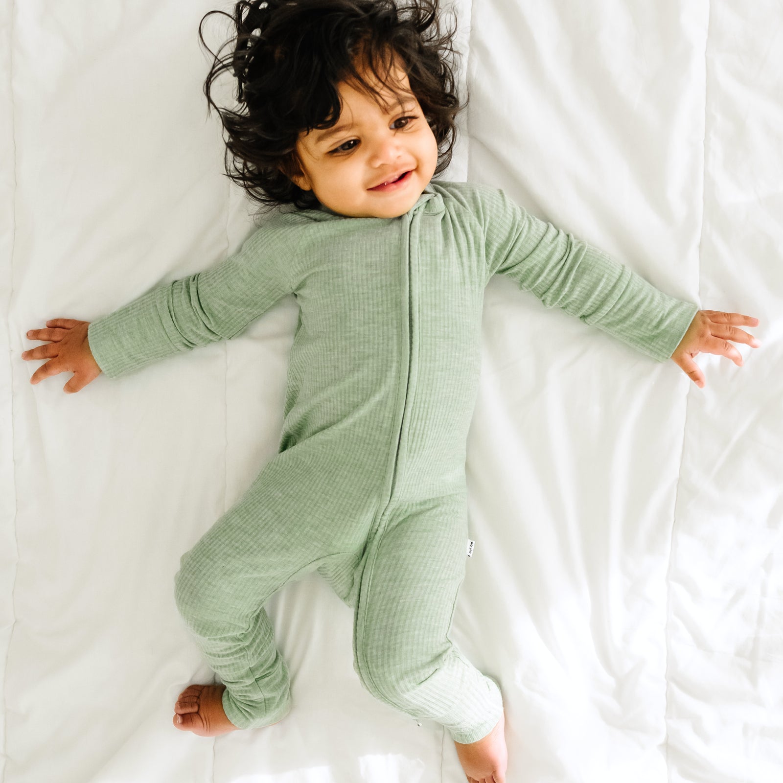 Child playing on a bed wearing a Heather Sage Ribbed zippy