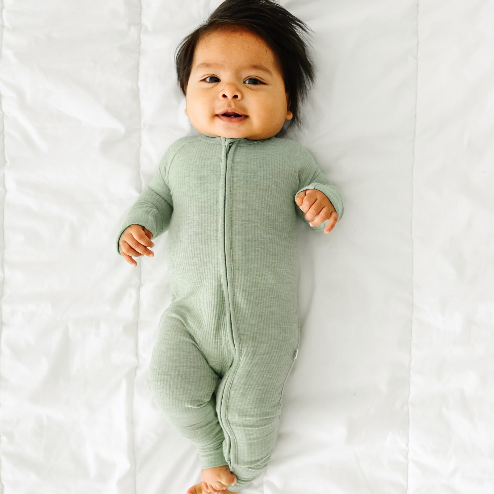 Child laying on a bed wearing a Heather Sage Ribbed zippy