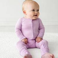 Child sitting on a bed wearing on a Light Orchid zippy