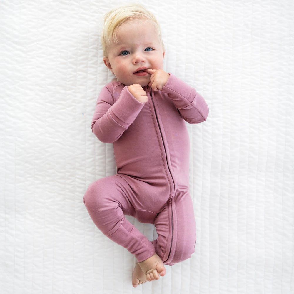 Child laying on a bed wearing a Cozy Dusty Plum zippy
