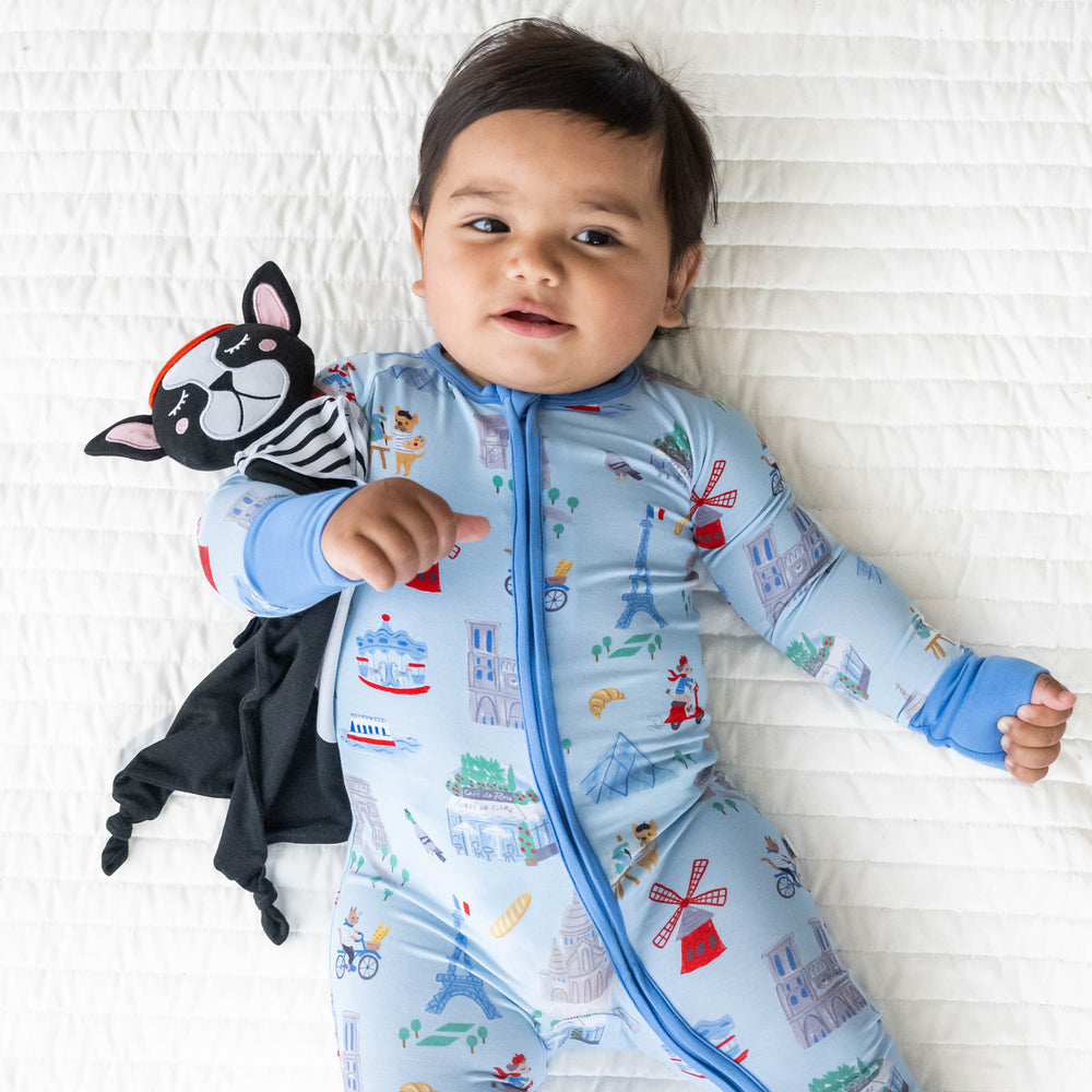 Top view image of baby laying down wearing the Blue Weekend in Paris Zippy and holding a Pierre the French Dog Sleepyhead Lovey