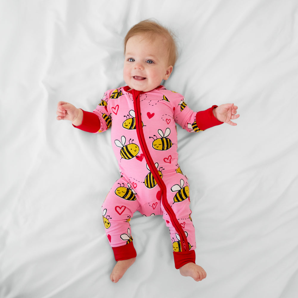 Image of a child laying on a bed wearing a pink Bee Mine zippy