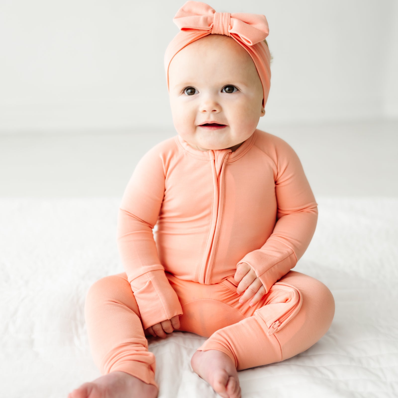 Child sitting wearing a Peach zippy paired with a luxe bow headband