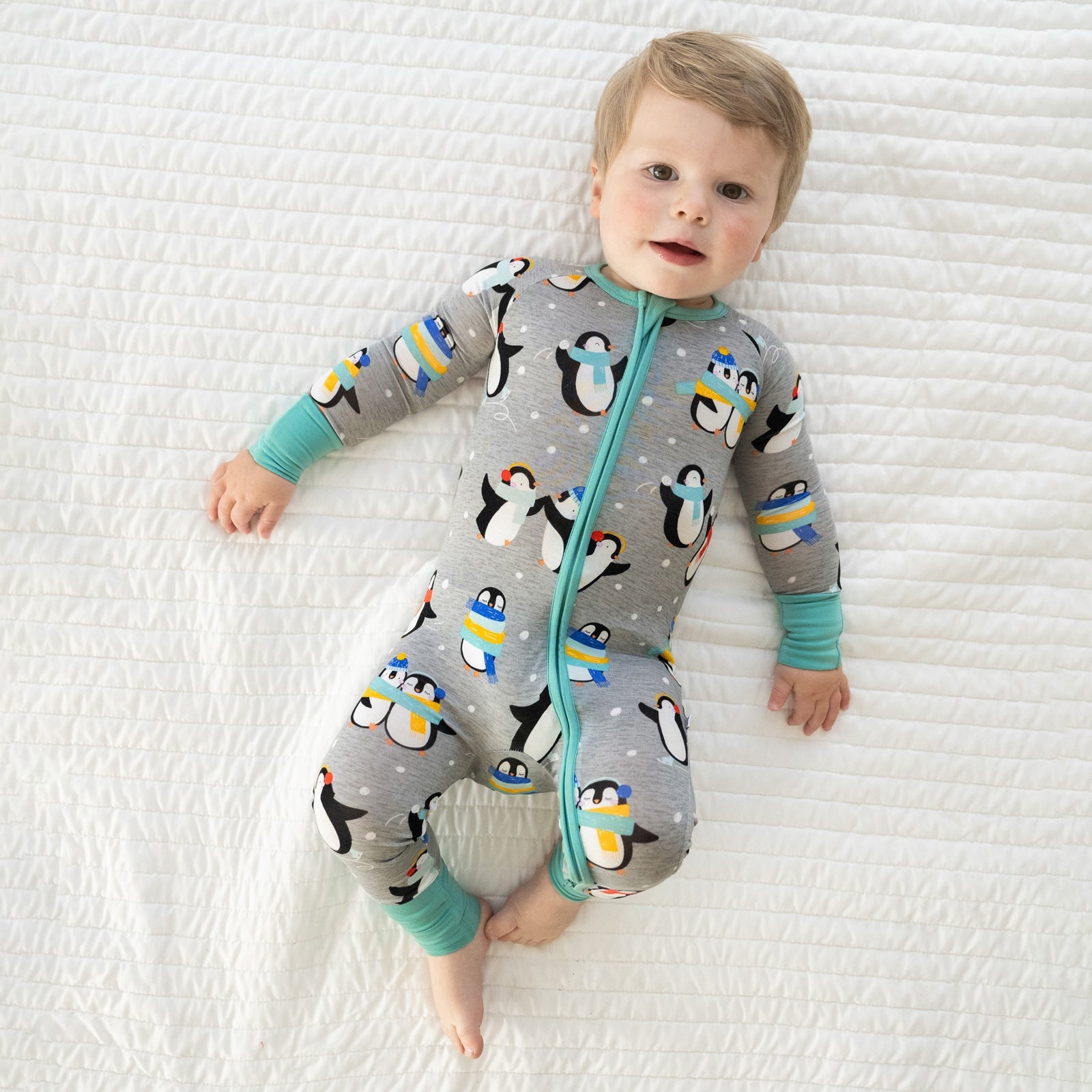 Child laying on a bed wearing a Penguin Party zippy