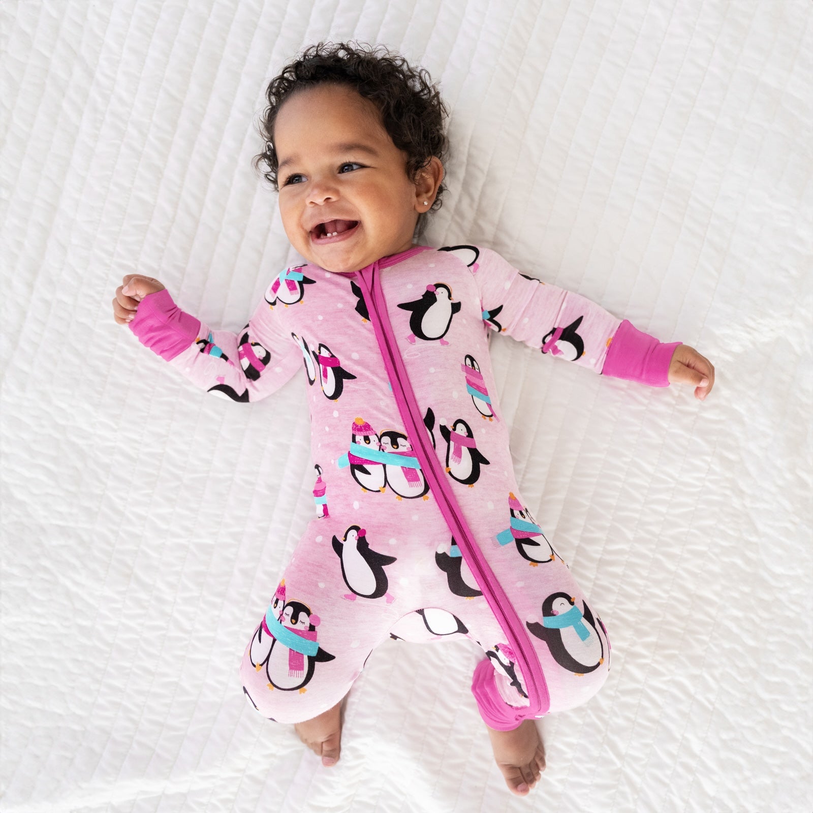 child laying on a bed wearing a Pink Penguin Party zippy