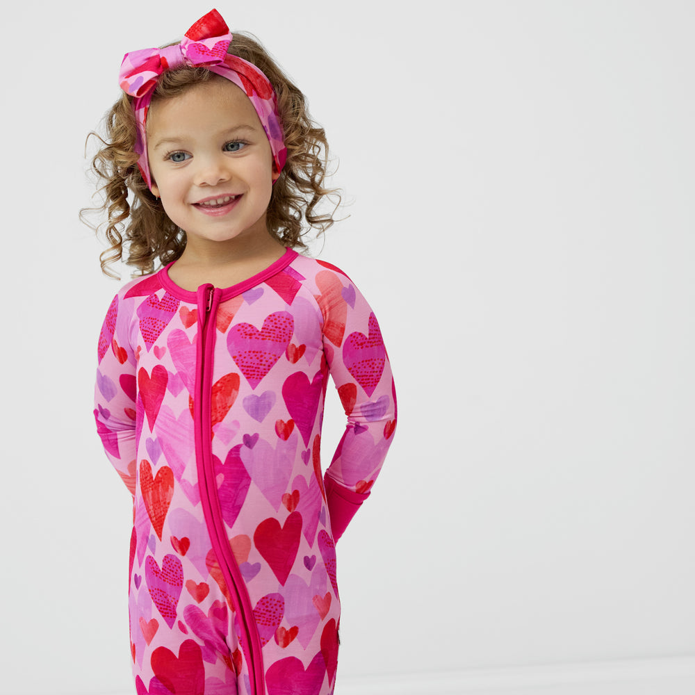 Girl wearing Pink Hearts & Crafts zippy pajamas with matching Luxe Bow Headband.