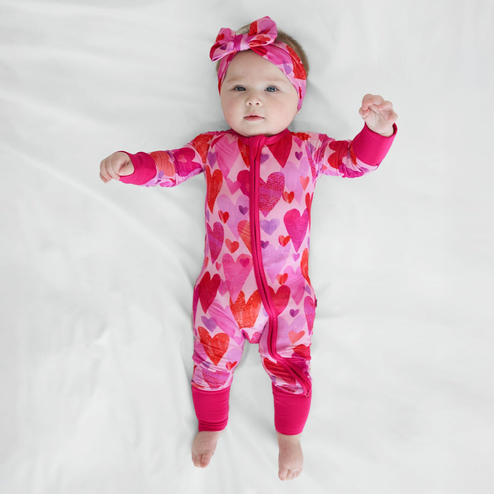 Baby wearing Pink Hearts & Crafts zippy pajamas with matching Luxe Bow Headband.