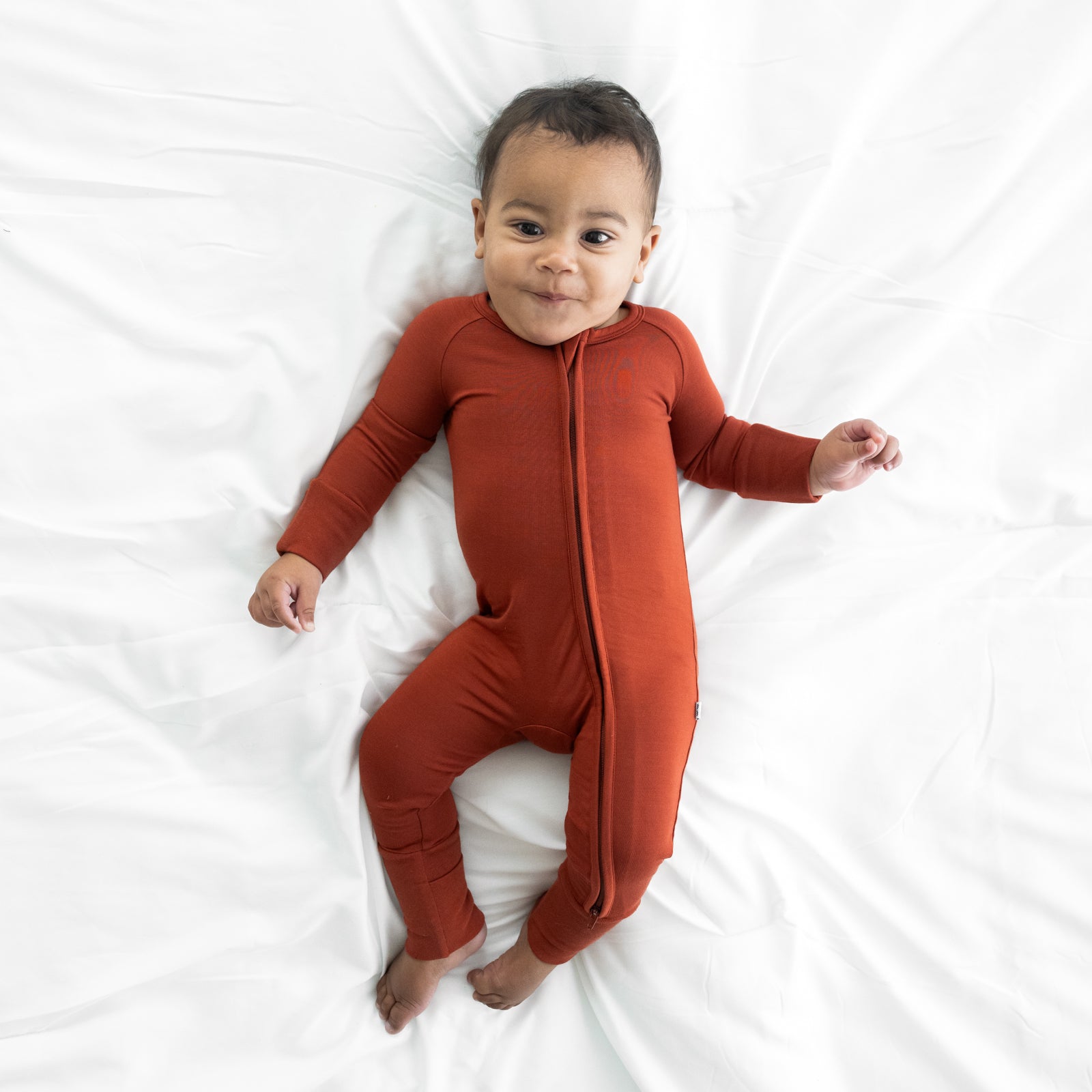 Child laying on a bed wearing a Cozy Rust zippy