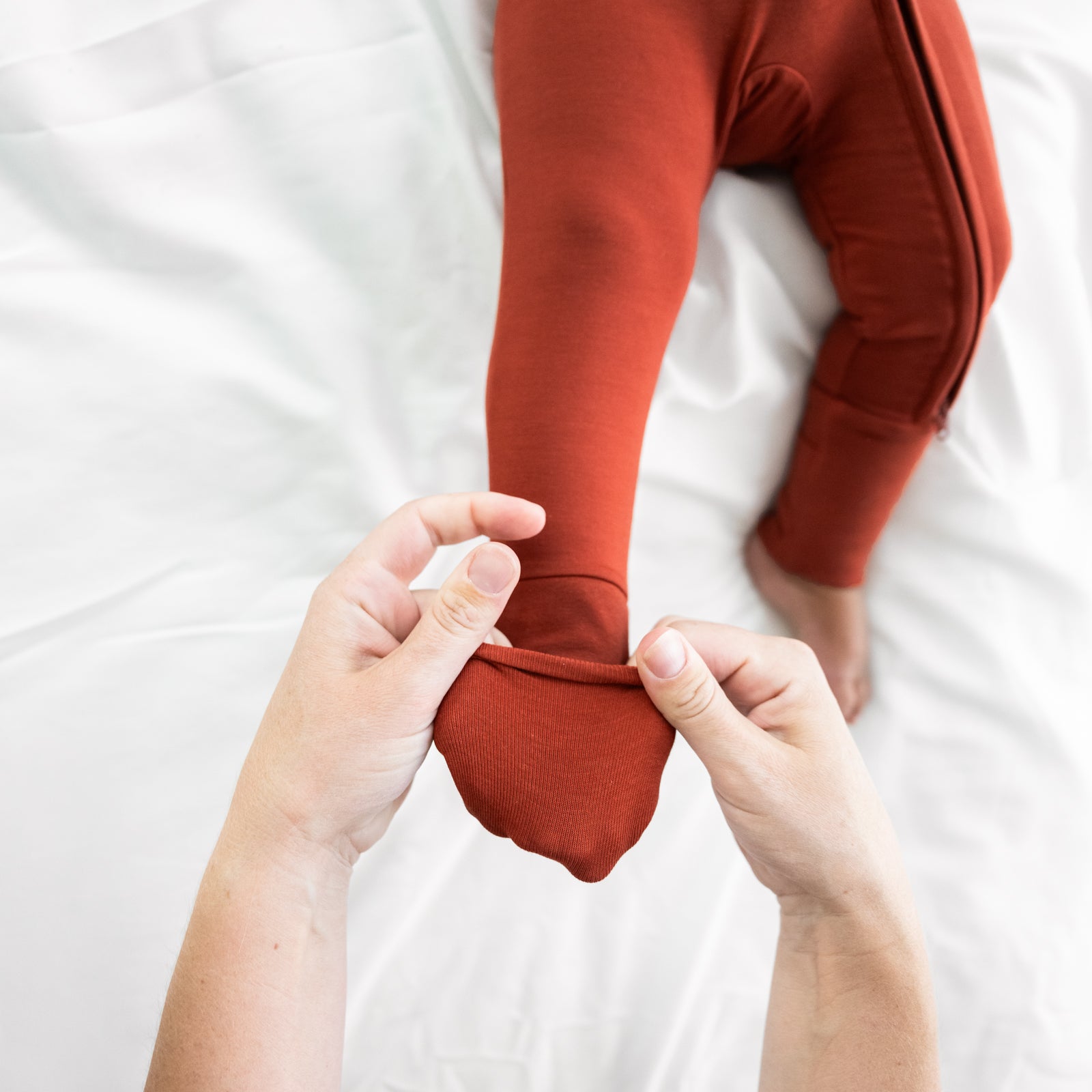 Child laying on a bed wearing a Cozy Rust zippy. Mom is showing the folded foot cuff