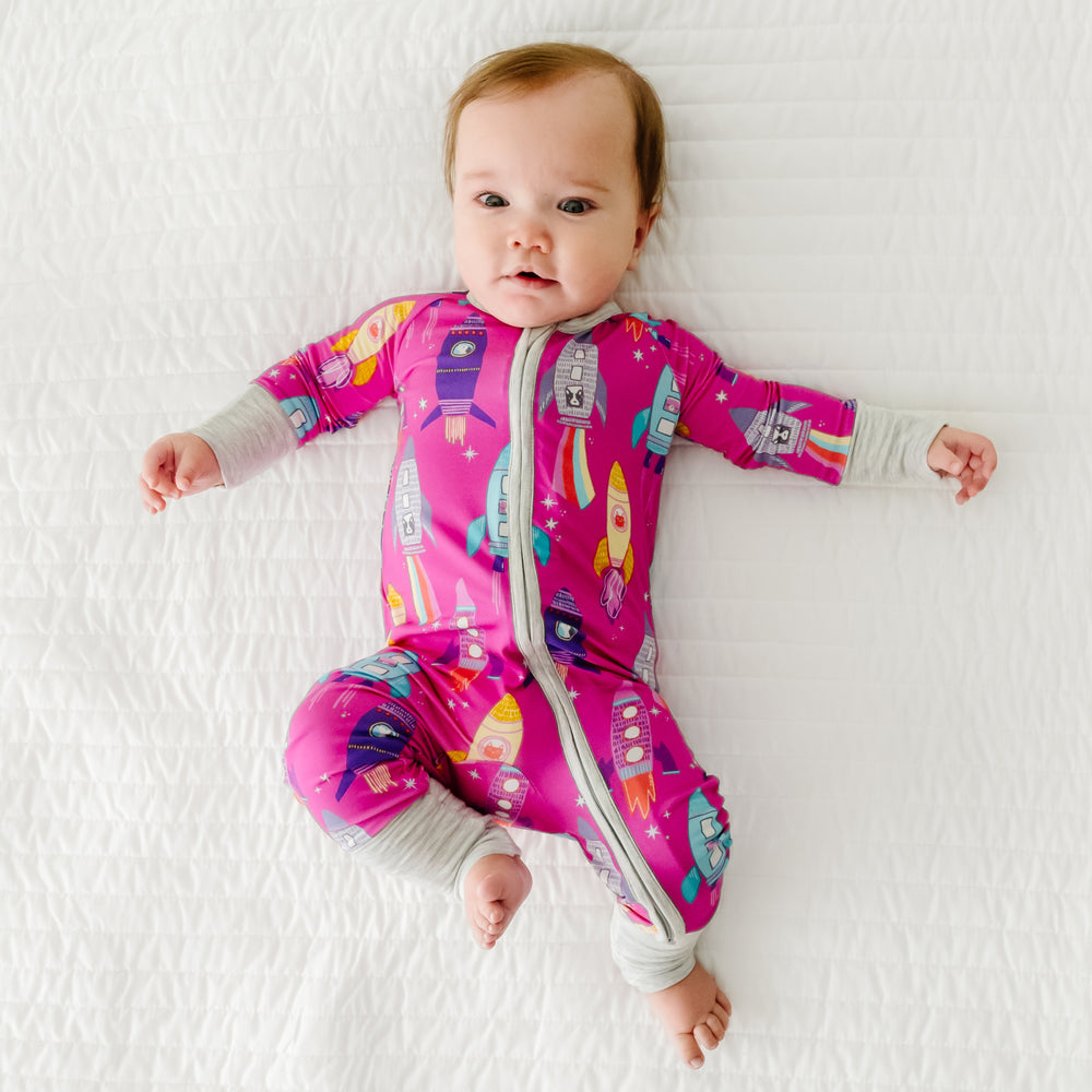 Child laying on a bed wearing a Pink Space Explorer zippy