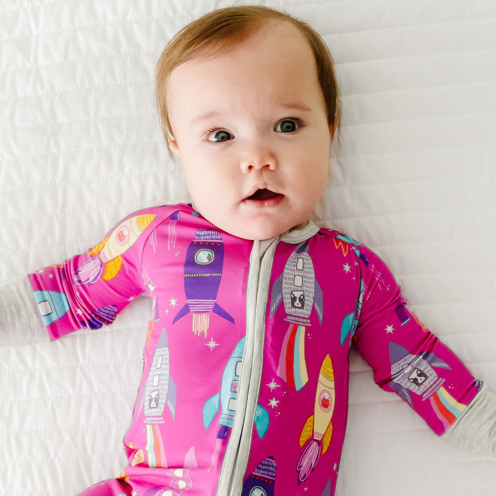 Close up image of a child laying on a bed wearing a Pink Space Explorer zippy