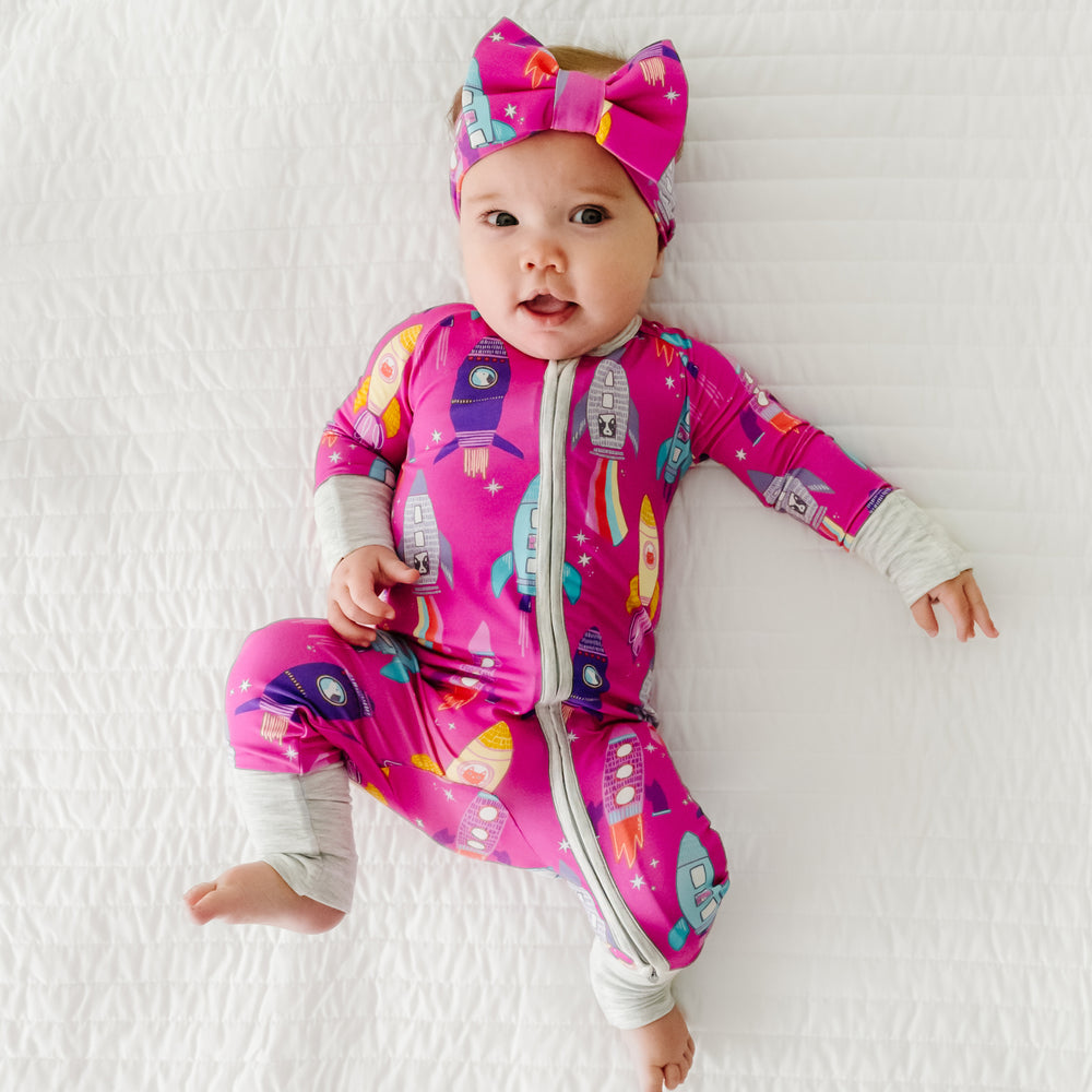 Child laying on a bed wearing a Pink Space Explorer zippy paired with a luxe bow headband