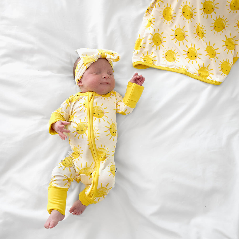 newborn baby wearing sunshine zippy and luxe bow with the matching blanket next to her