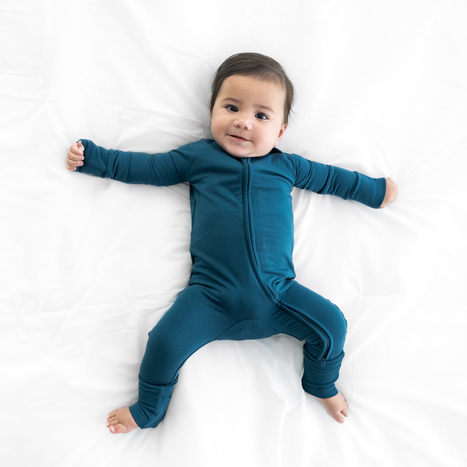 Child laying on a bed wearing a Cozy Twilight Teal zippy