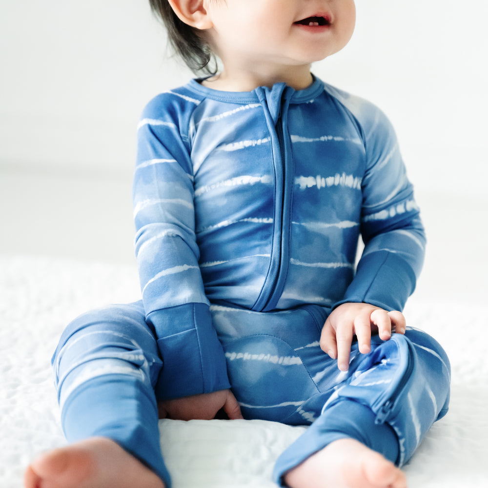 Close up image of a child sitting on the ground wearing a Blue Tie Dye Dreams zippy