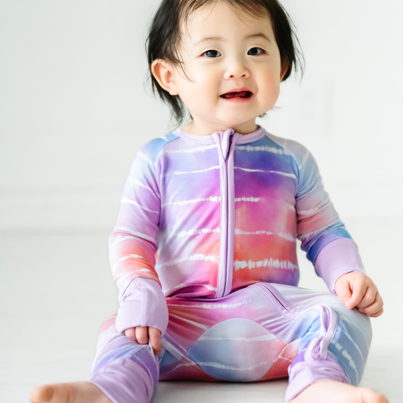 Child sitting on the ground wearing a Pastel Tie Dye Dreams zippy