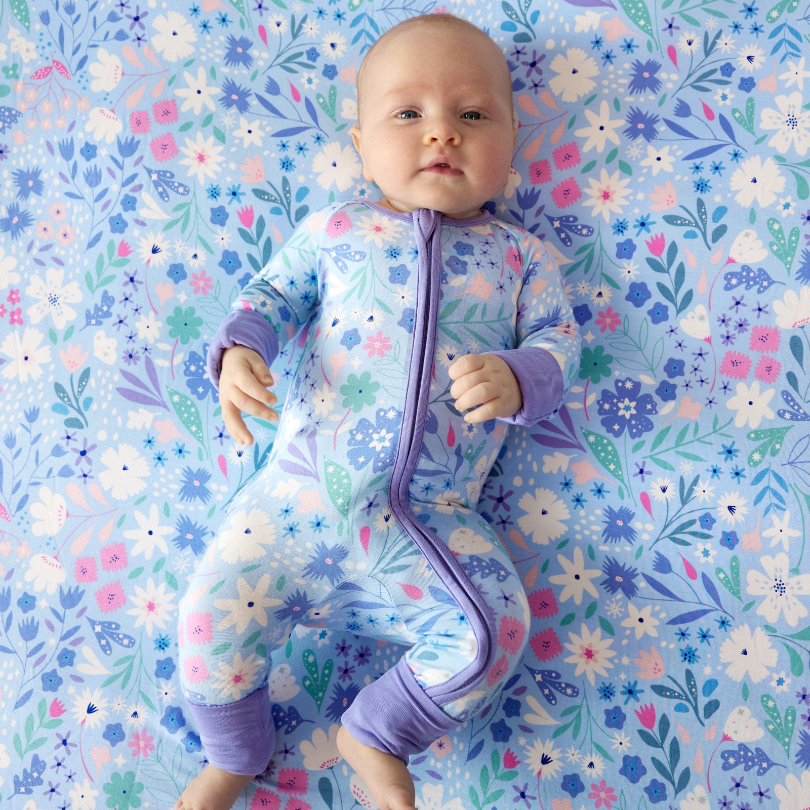 Image of a child laying on a Magical Meadow crib sheet wearing a matching zippy