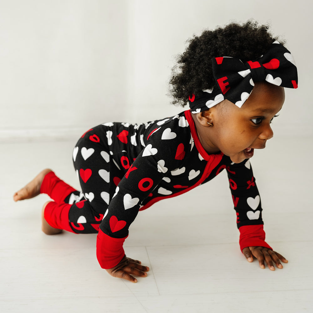Click to see full screen - Image of a child crawling wearing a Black XOXO zippy paired with a matching luxe bow headband
