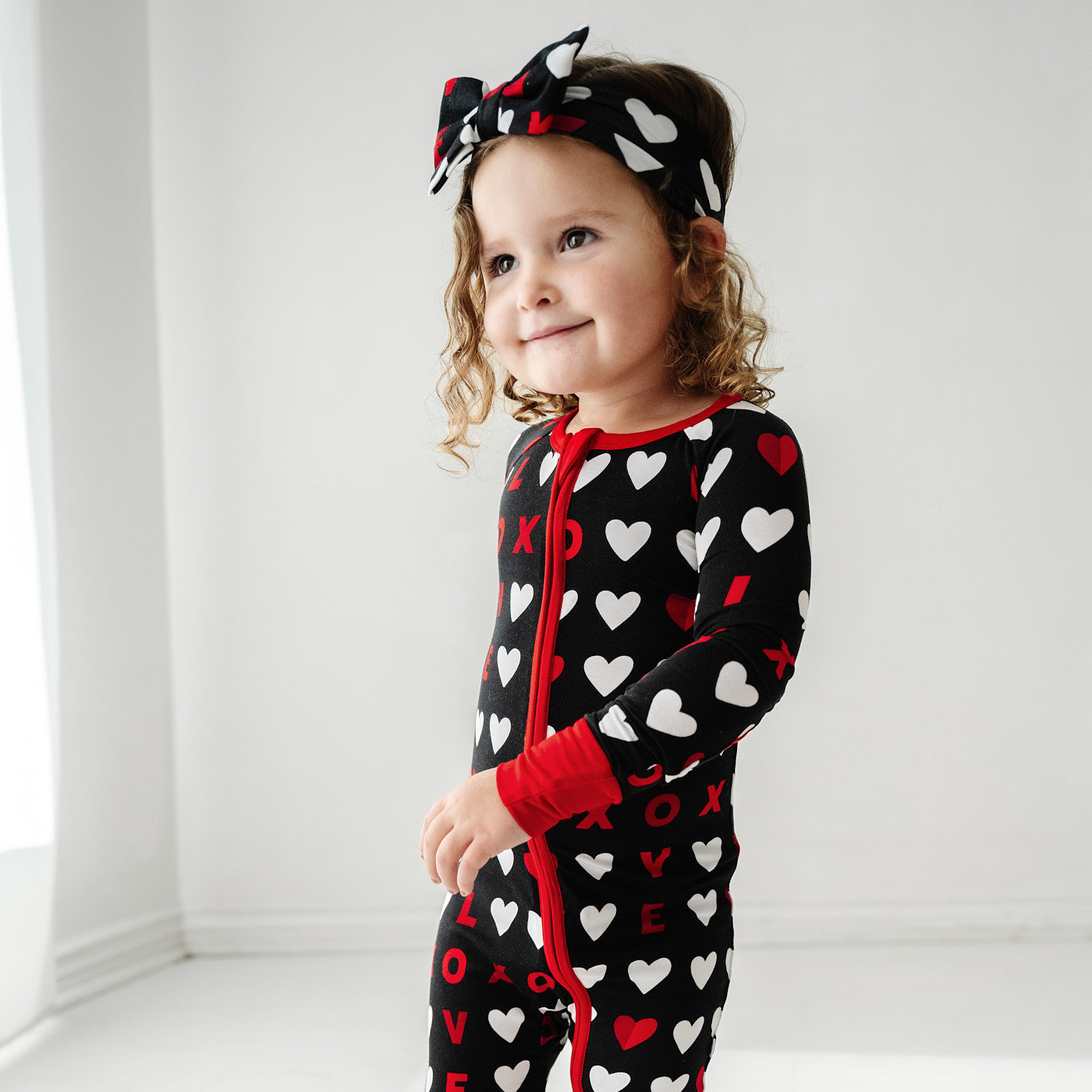 Close up image of a child posing wearing a Black XOXO zippy paired with a matching luxe bow headband