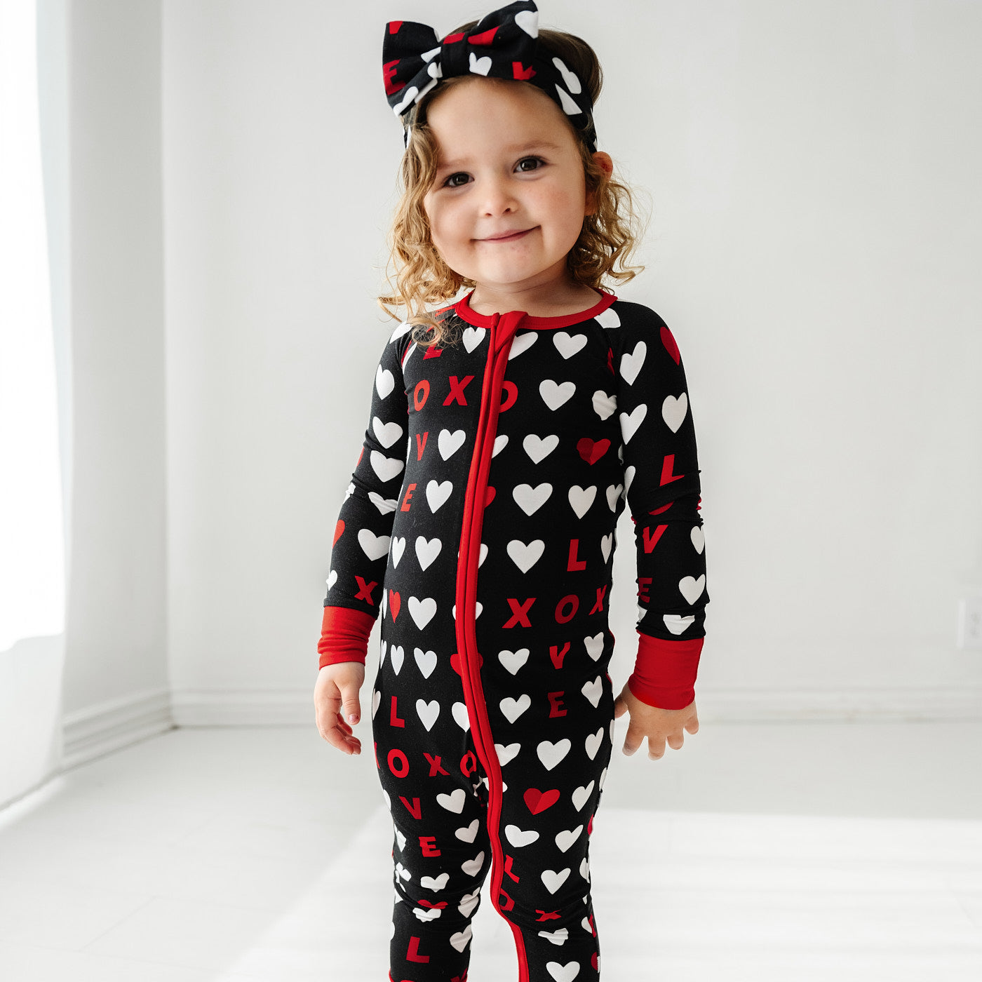 Image of a child posing wearing a Black XOXO zippy paired with a matching luxe bow headband