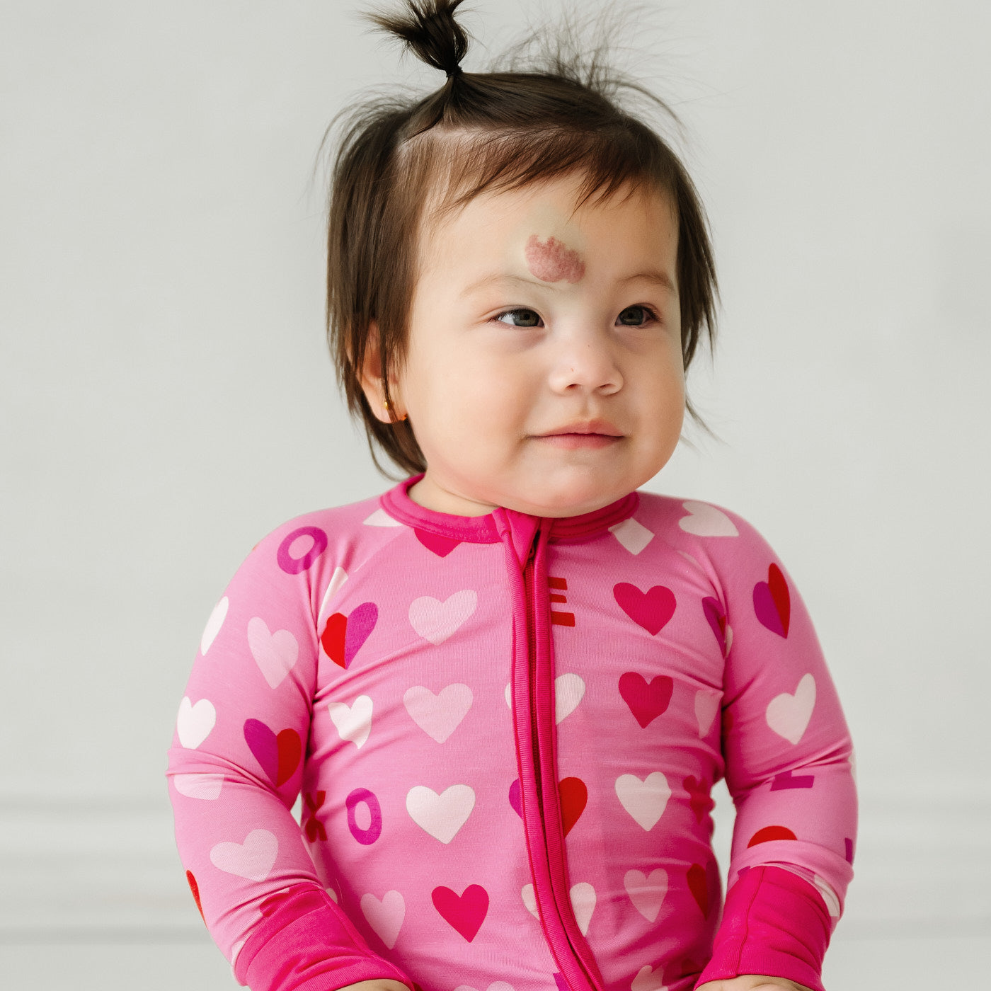 Close up image of a child sitting wearing a Pink XOXO zippy